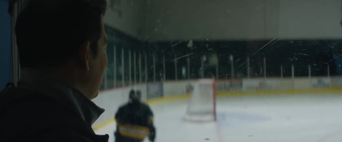 A man smiles as he watches his kid skate and practice at an ice hockey rink