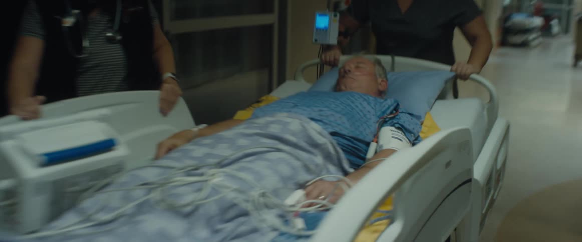 A woman walks past a patient being transported in a hospital bed by three nurses