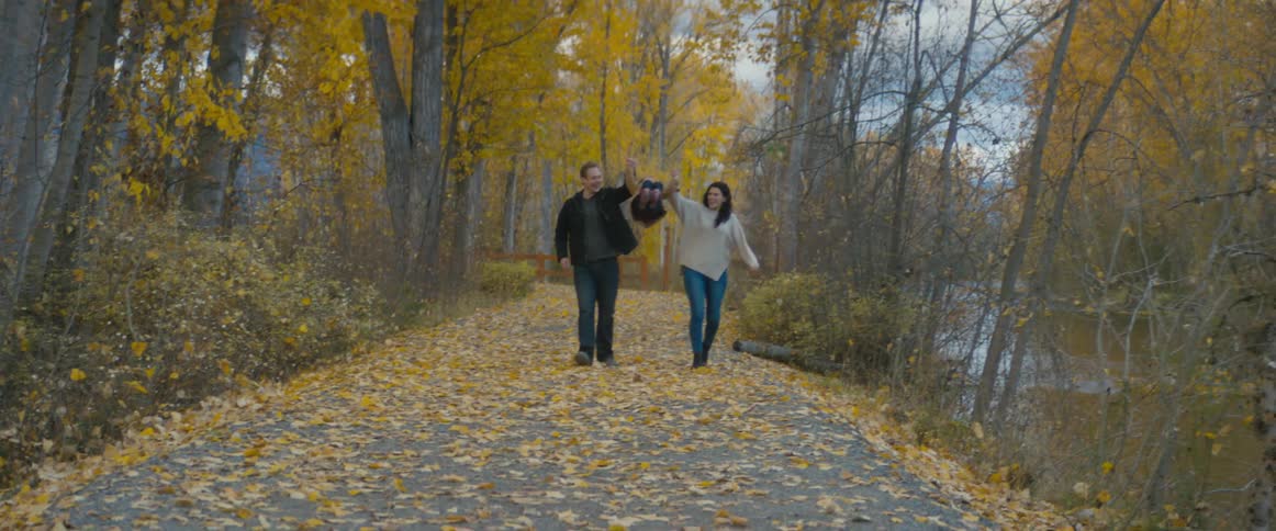Parents walk holding hands with their daughter on a path near a river on a park at autumn