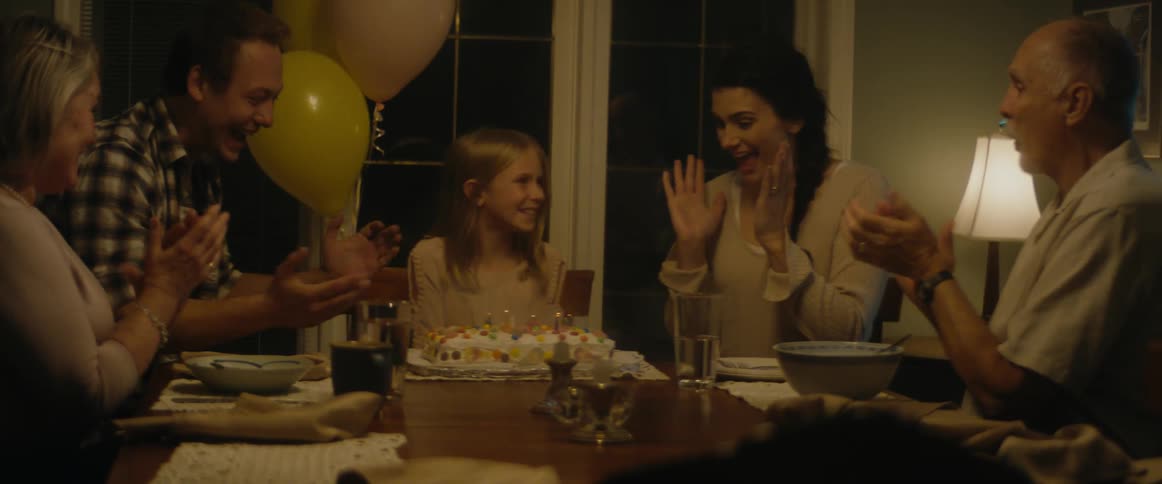 Family claps their hands as birthday girl blows out candles on birthday cake