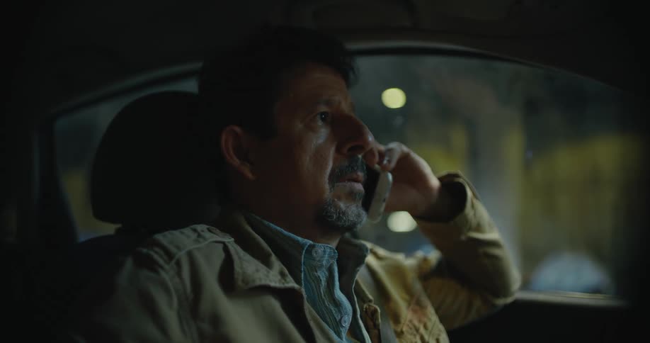 Tired disappointed man tries to make a call on his smartphone while sitting inside a parked carat night