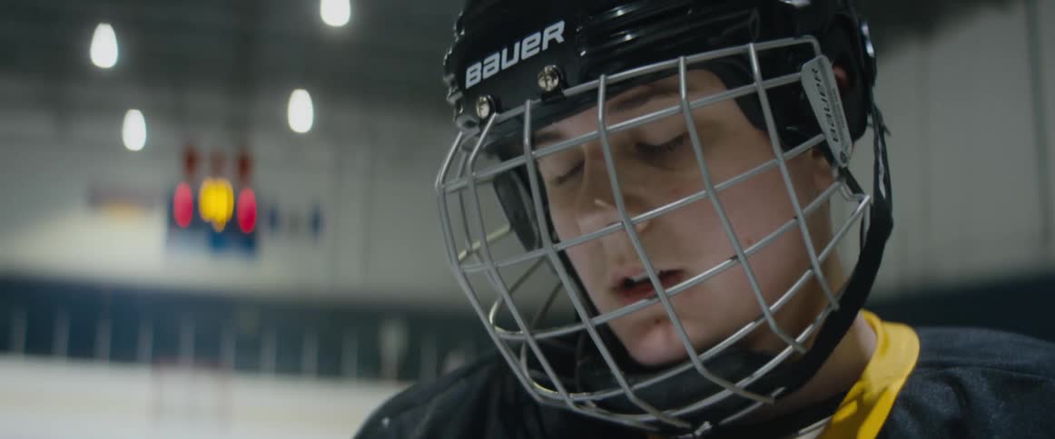 A hockey player is standing on the ice wearing a helmet with a face guard