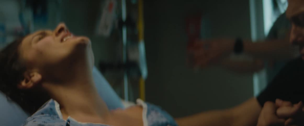 A man kisses his wifes hand as she grimaces in pain while giving birth
