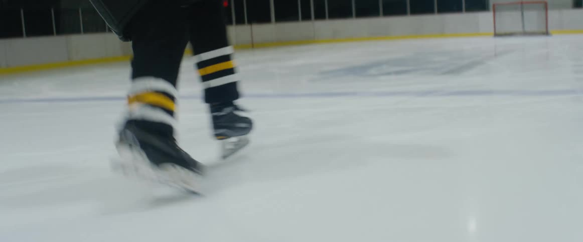 A hockey player is moving the puck across the ice with a hockey stick and puts it in the goal