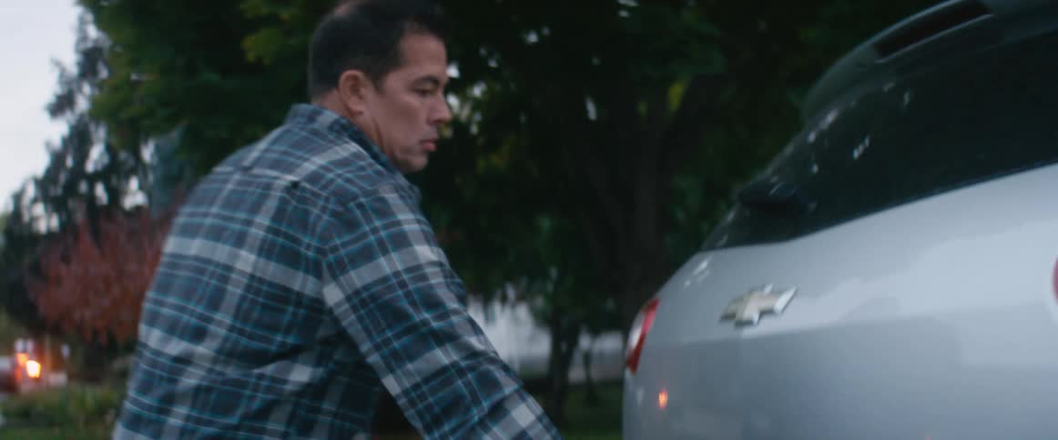 A man puts a duffle bag into the back of an automobile and a teenage boy gets into the passenger side