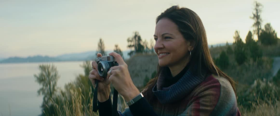 Woman looking at a lake turns around to take a picture at evening