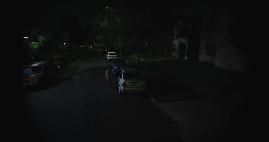 Man gets into car with blinking lights that is parked on street in neighborhood