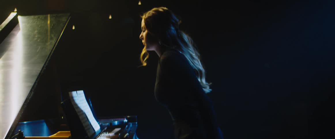 A pianist walks across a stage to sit before her piano