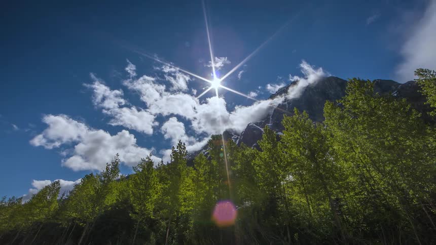 Timelapse of clouds floating over trees and a mountain