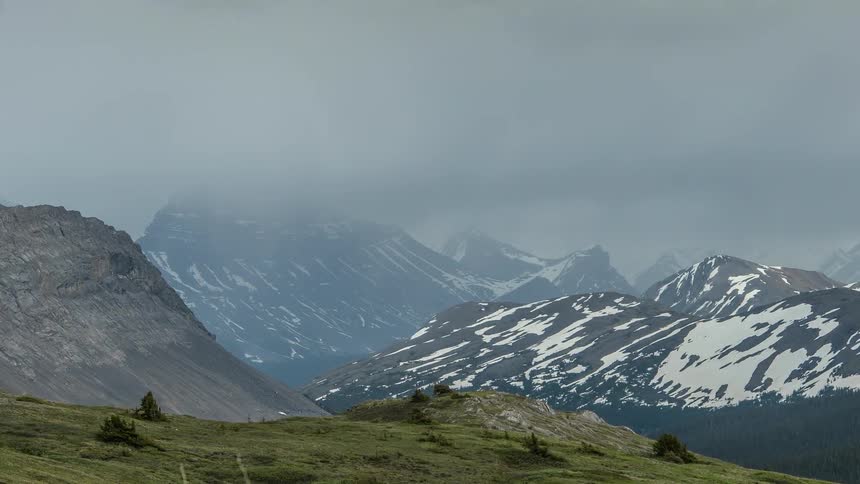 A mountain range is covered with grass and snow in the distance on a cloudy day