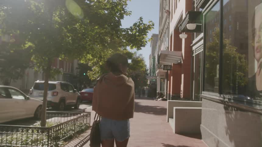 A woman walks along a sidewalk in a city during the day