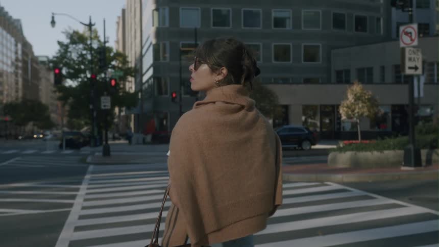 A woman standing on a city sidewalk looking at traffic waiting to cross the street