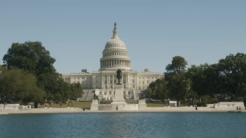 A few tourists walk near the water with the us capitol building behind them