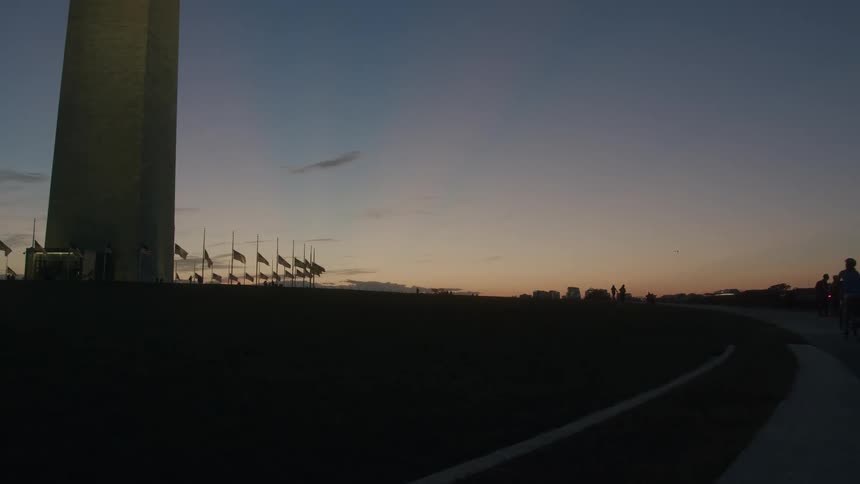 People bike past a monument as the sun sets