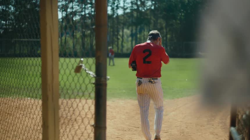 A baseball player takes a glove and puts on his cap and he walks out onto the field