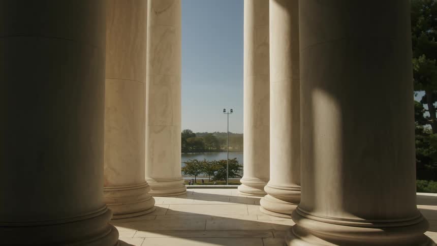 A building with tall and wide columns overlooks a pond