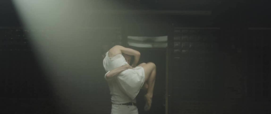 A man and woman practice a modern dance under a flashing light in a dim room