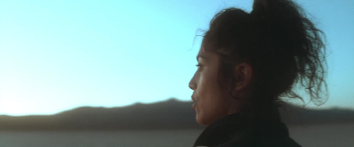 Woman with curly hair and black jacket walks in the desert at sunset talking