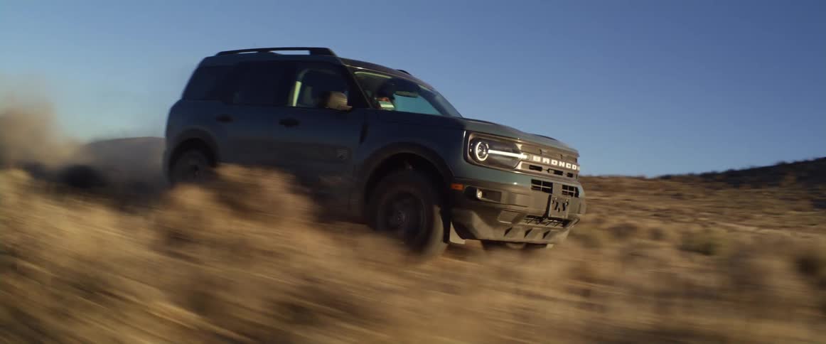 A vehicle kicks up dirt as it speeds through a field filled with shrubs