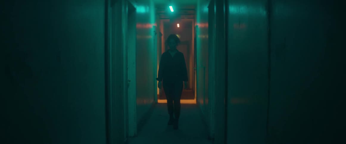 A woman sings to herself while walking down a dark hallway
