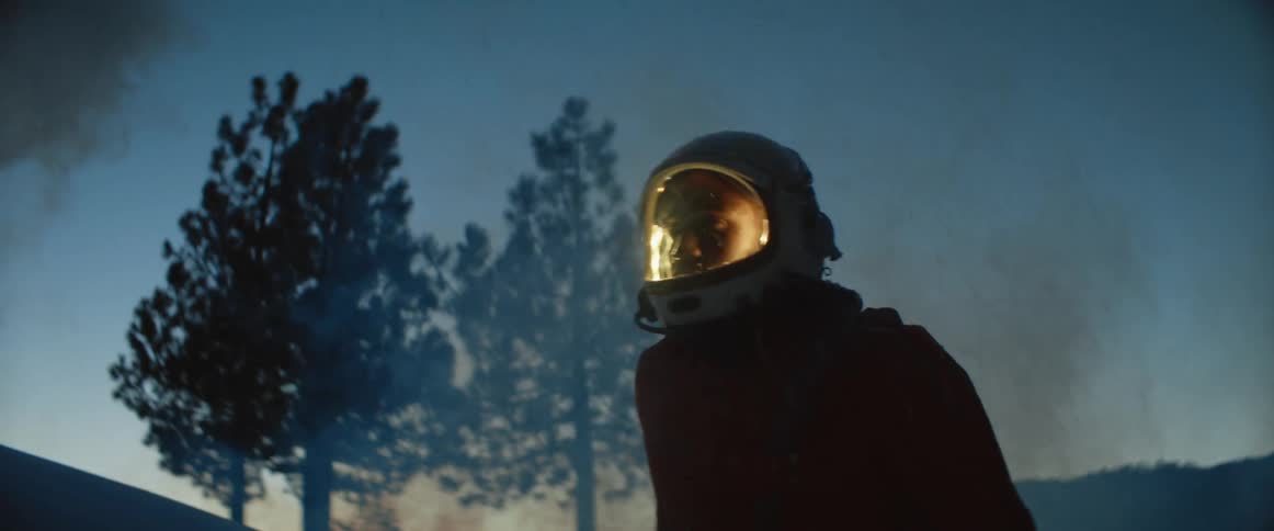 A man in a helmet and jumpsuit walks through a smoke filled forest