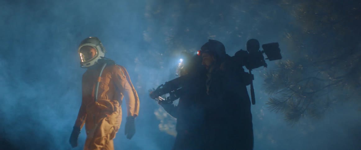 A film crew follows a man in a space suit in the dark