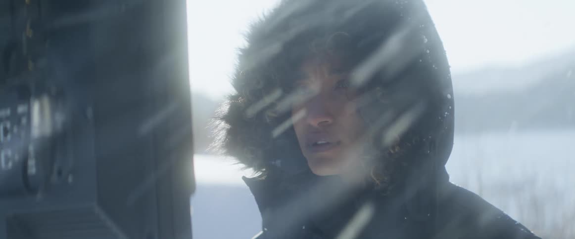 A woman watches a television screen outdoors as heavy snow falls around her