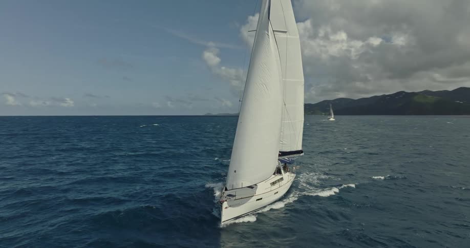 Sailboat tows inflatable boat as it sails across ocean with coast in the background