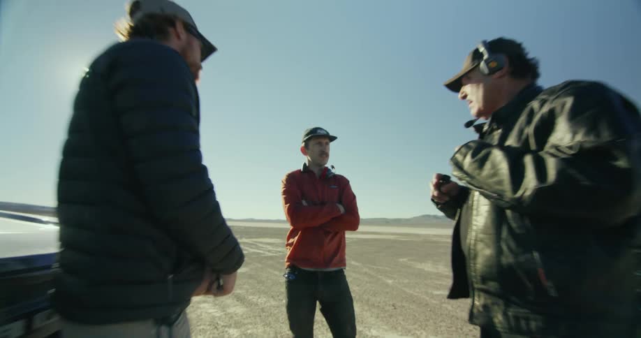 Men stand near car parked in desert on sunny day and hold discussion