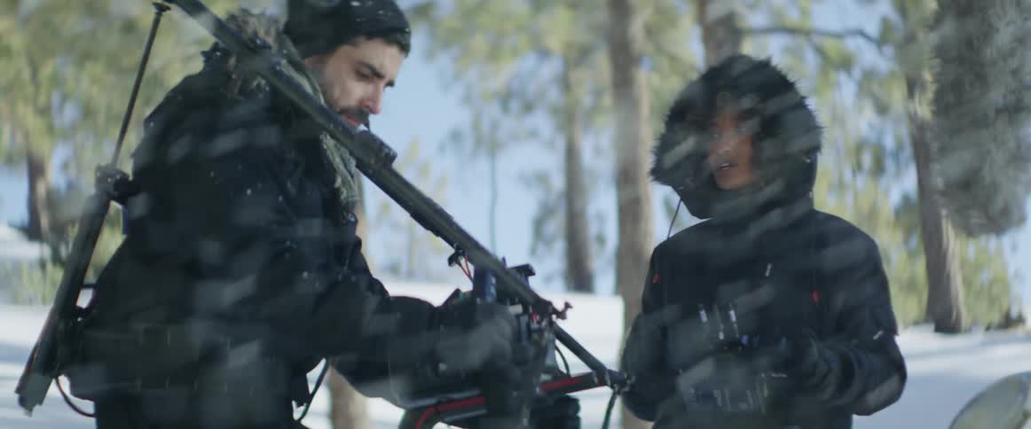 Film crew members smile and talk while working on set in snow covered forest