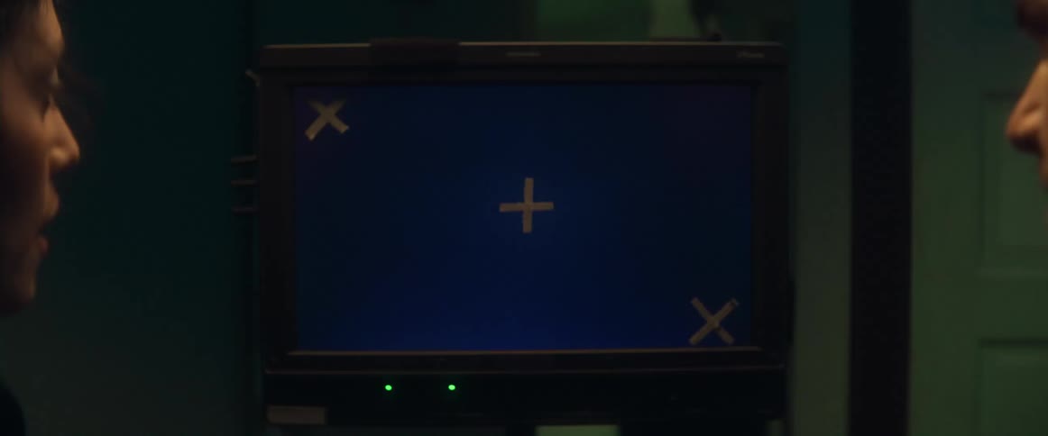 A man and a woman are in a dark room looking at a computer monitor as people walk past them