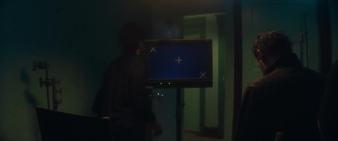 A small group watches a monitor while others walk in and out of the room