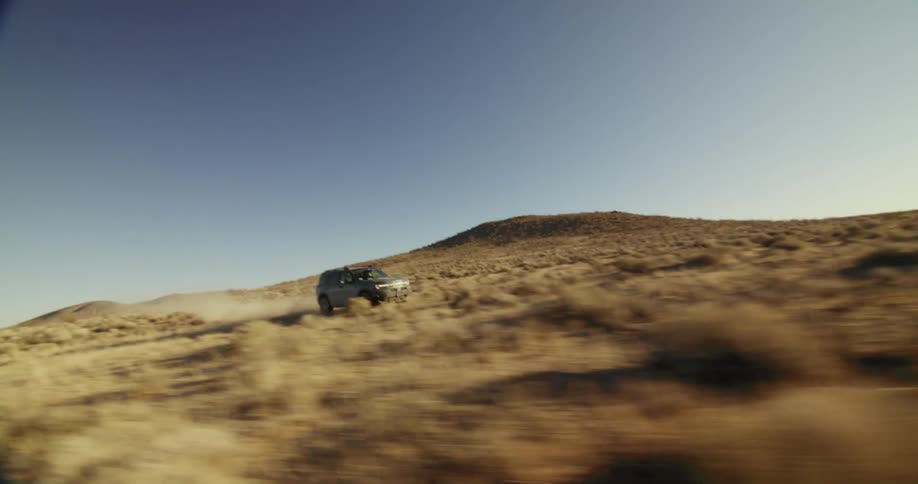 A truck is traveling across the desert and there are mountains in the distance