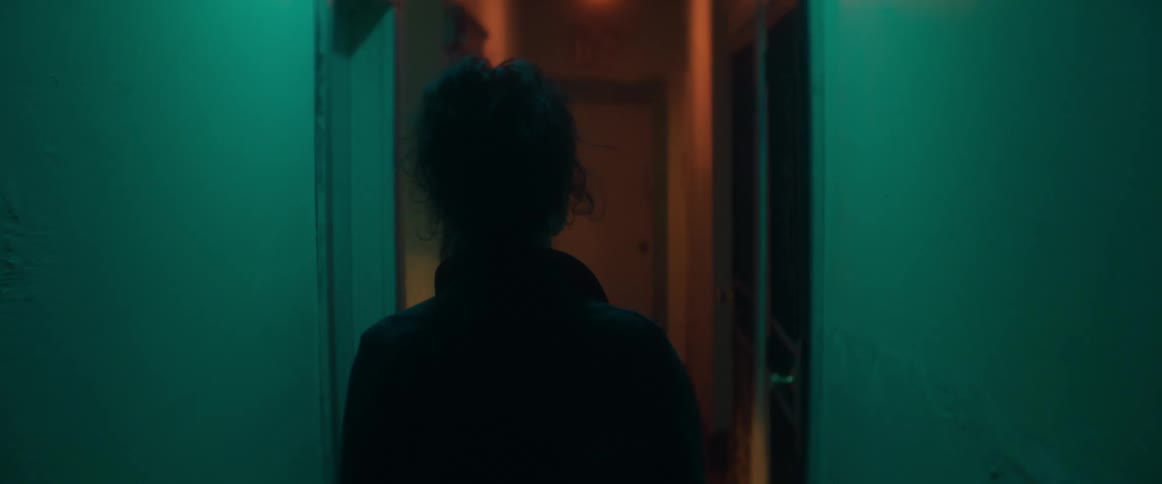 A woman sings while walking down a narrow hallway in an apartment building