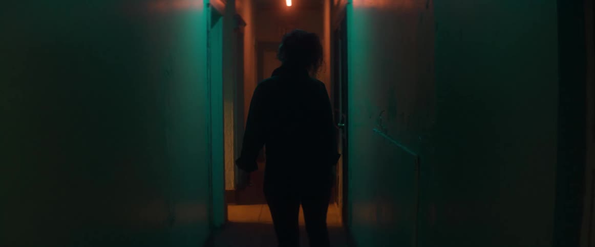 A woman looks up and around while walking down a dim hallway