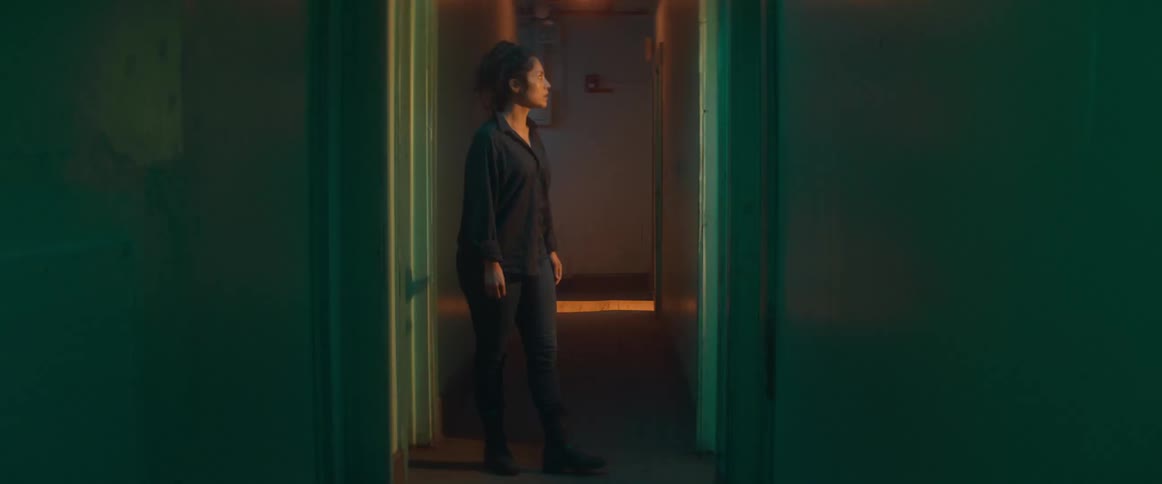 A woman walks down a dim hallway and into a glowing light filled apartment