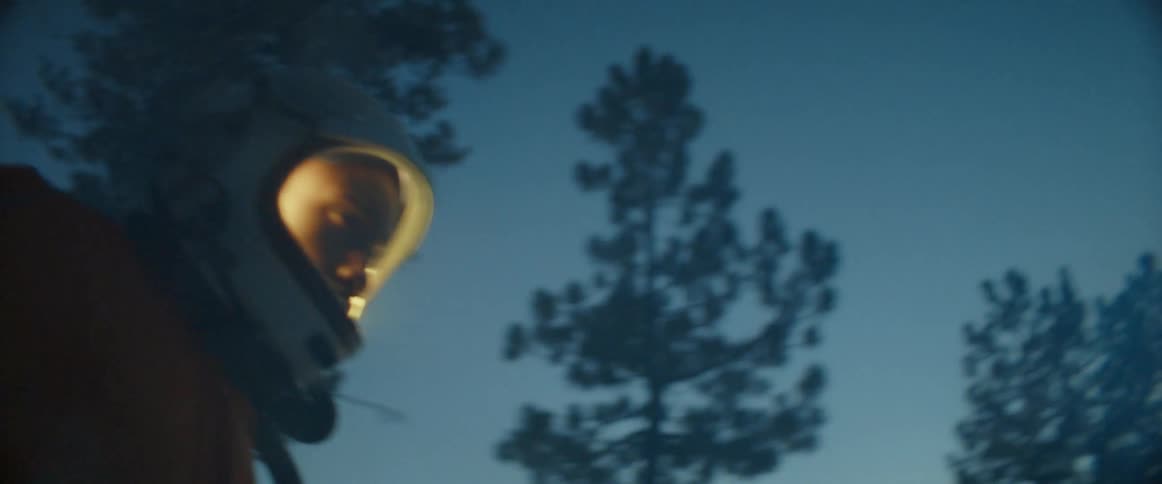 A man wearing a glowing helmet walks through a forest as snow falls