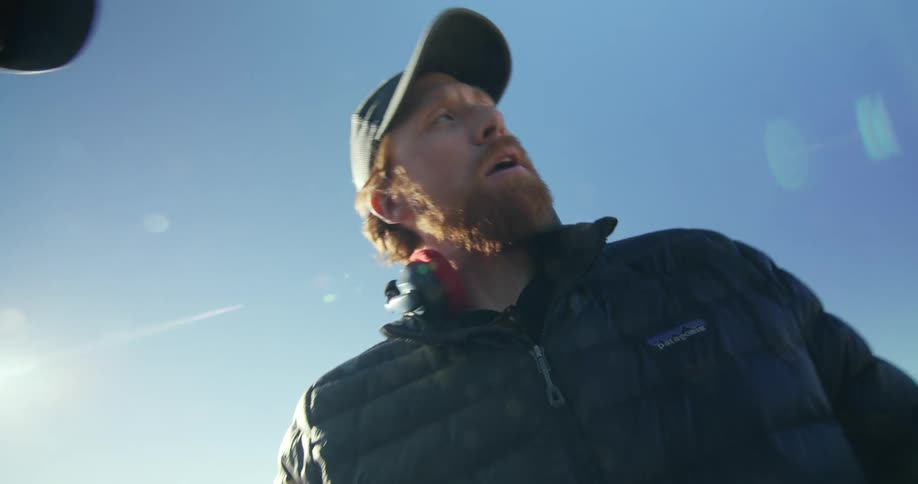 Standing ondesert plain redheaded man gives directions using two toy cars