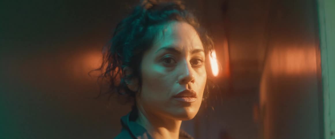 A woman walks into an apartment building hallway and turns her head as she goes into a doorway