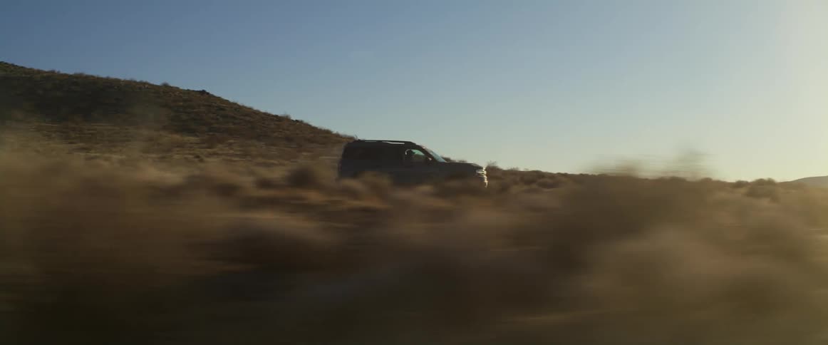 The sun shines brightly upon a truck traveling across the desert