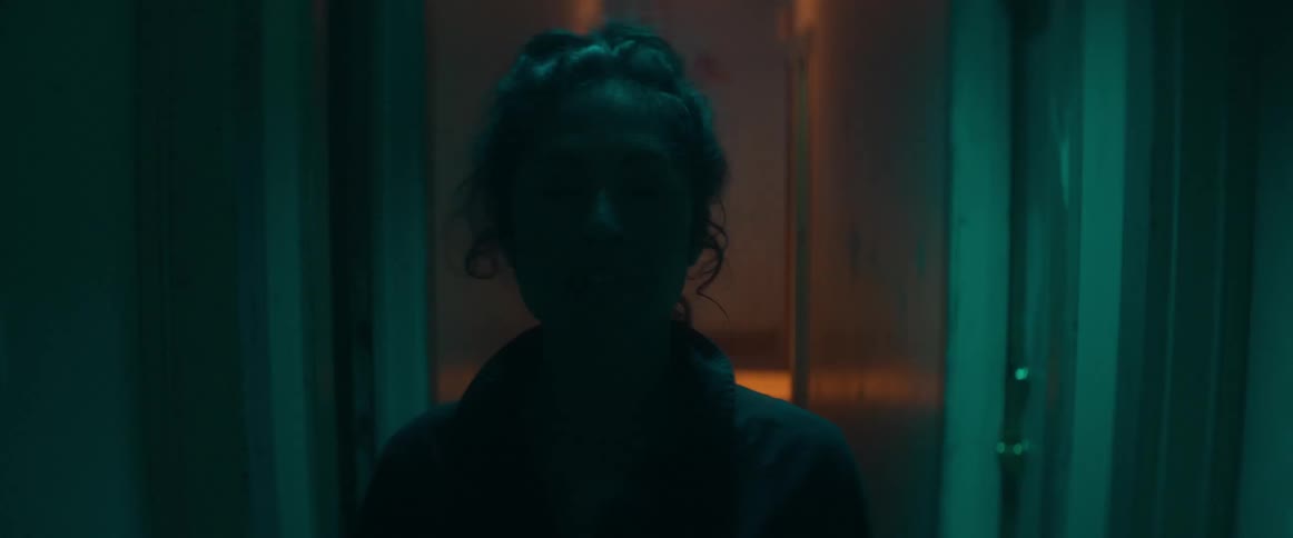A woman looks around nervously while walking down a dim hallway