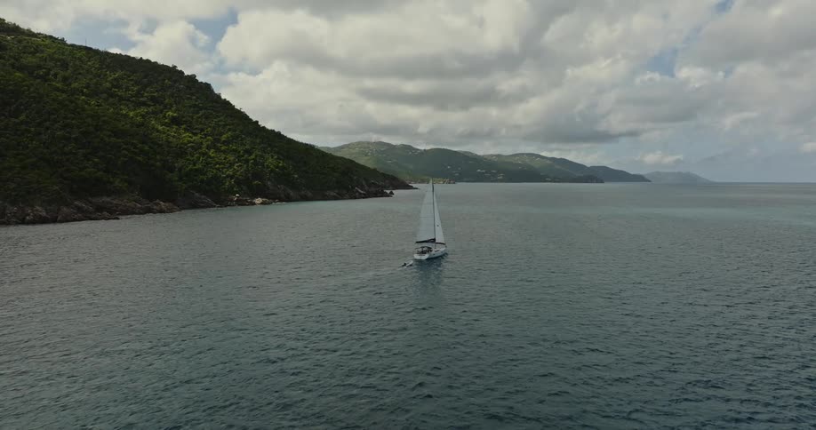 A sail boat floats in the water near shore and there is a smaller boat behind it