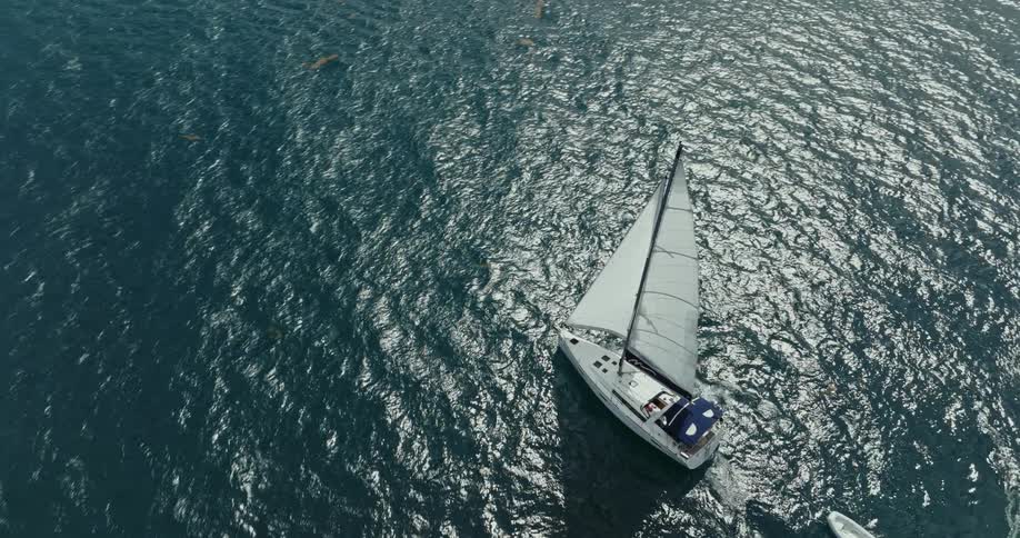 A sailboat towing a dingy sails on the shimmering water