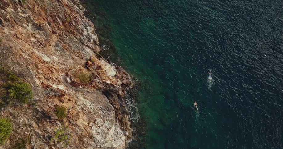 Aerial view of two people swimming in the water along the coast