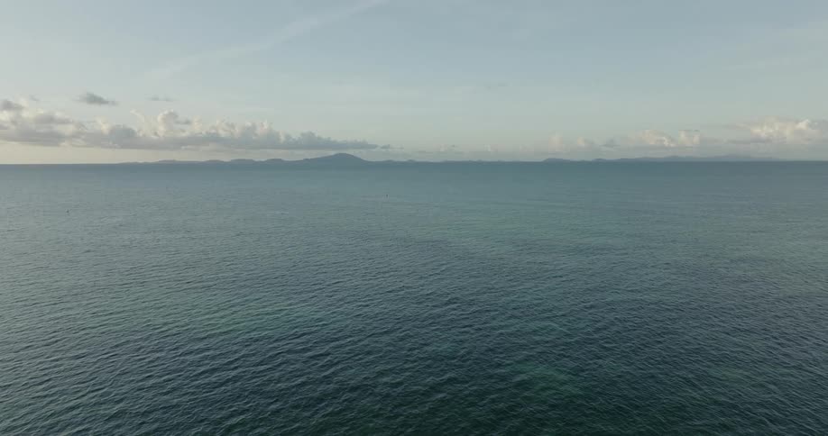 Sunlight reflects on the water as it ripples and waves and clouds hang over mountains in the distance