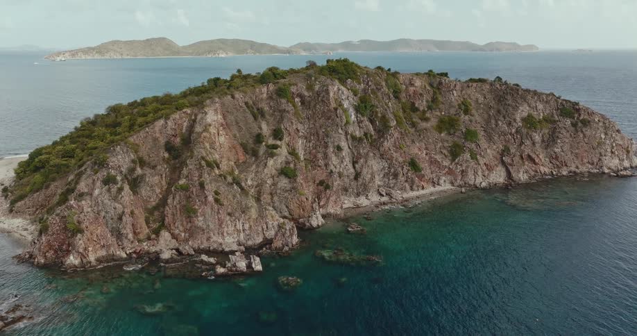 A mountainous island on the ocean during the day