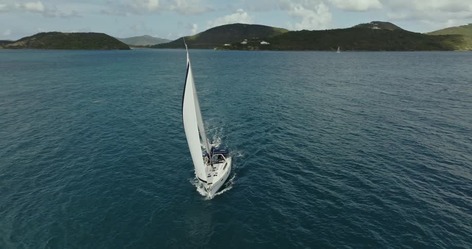 A sailboat sails across the ocean while towing a smaller boat behind it