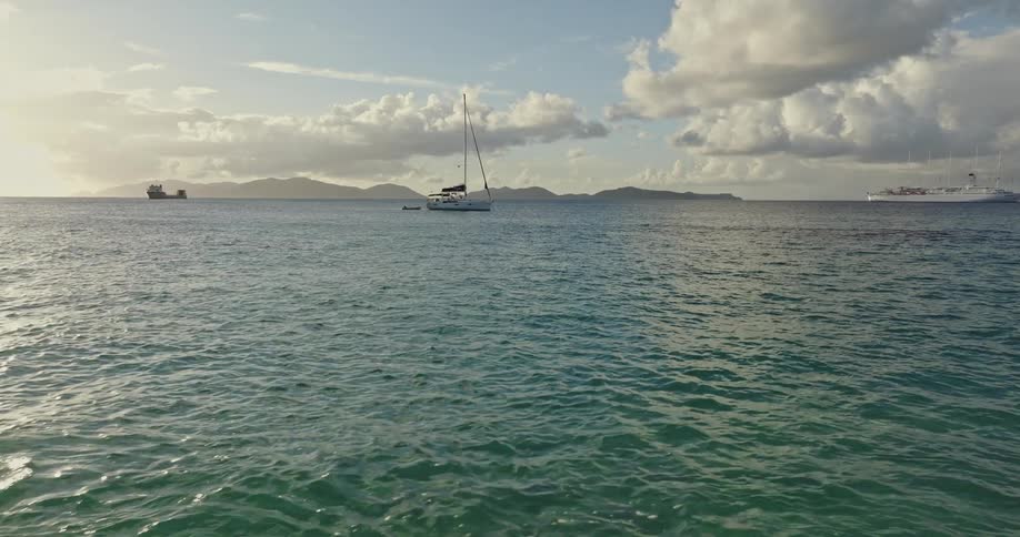 Cruise ship and sailboat float on ocean between two coasts on a cloudy day