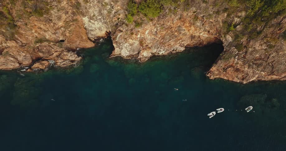 People swimming back towards small boats away from the rocky cliff