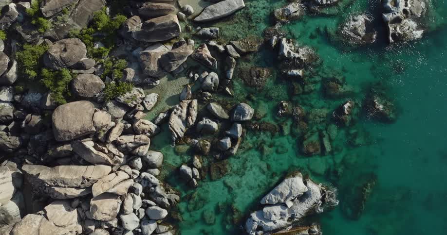 Aerial view of a rocky shoreline with clear water sparkling in the sunlight